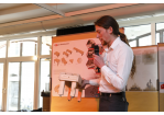 Aktion Sondermöbel - Foto einer Veranstaltung - vor einer Infowand mit einer Miniaturausgabe eines Modells in der Hand am Mikrofon Lukas Zeidler