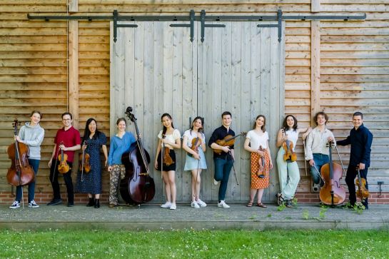 Fotografie – die LGT Young Soloists vor einem Holztor