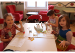 Drei Kinder sitzen um einen Tisch, kämmen sich die Haare und lackieren sich die Fingernägel.