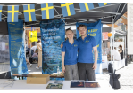 Zwei junge Personen stehen Arm in Arm in einem Pavillon der Schwedischen Botschaft. Am Pavillon ist eine Schnur mit vielen kleinen Schweden-Fahnen befestigt