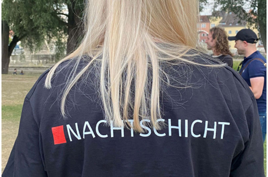 Fotografie: Eine Frau trägt ein T-Shirt mit der Rückenaufschrift „Nachtschicht“.