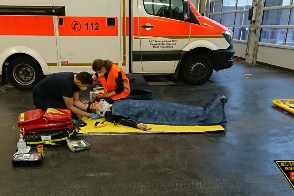 Fotografie: Teilnehmer einer Rettungssanitäter-Abschlussprüfung bei der Versorgung eines am Boden liegenden Patienten.