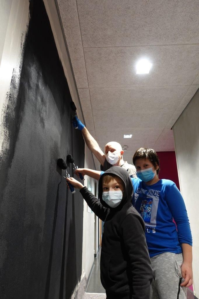 Auf dem Foto sind zwei Kinder und ein Erwachsener zu sehen, welche eine Wand streichen.