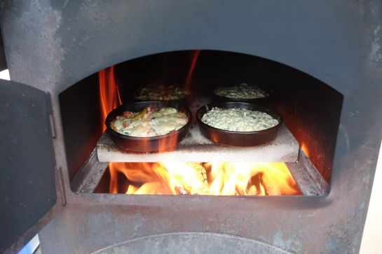Fotografie - Pizzen backen im Pizzaofen, der mit Holz beheizt wird 