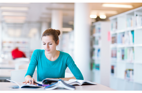Fotografie: Eine Frau sitzt mit Büchern an einem Tisch.