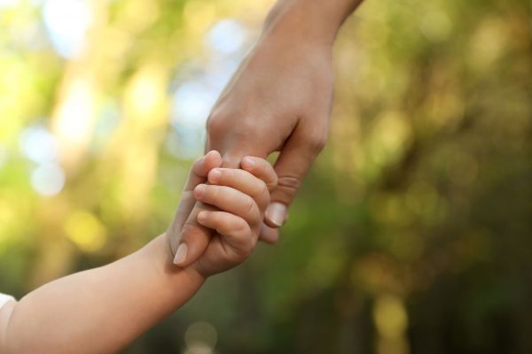 Fotografie: Eine Kinderhand hält den Finger einer erwachsenen Hand.