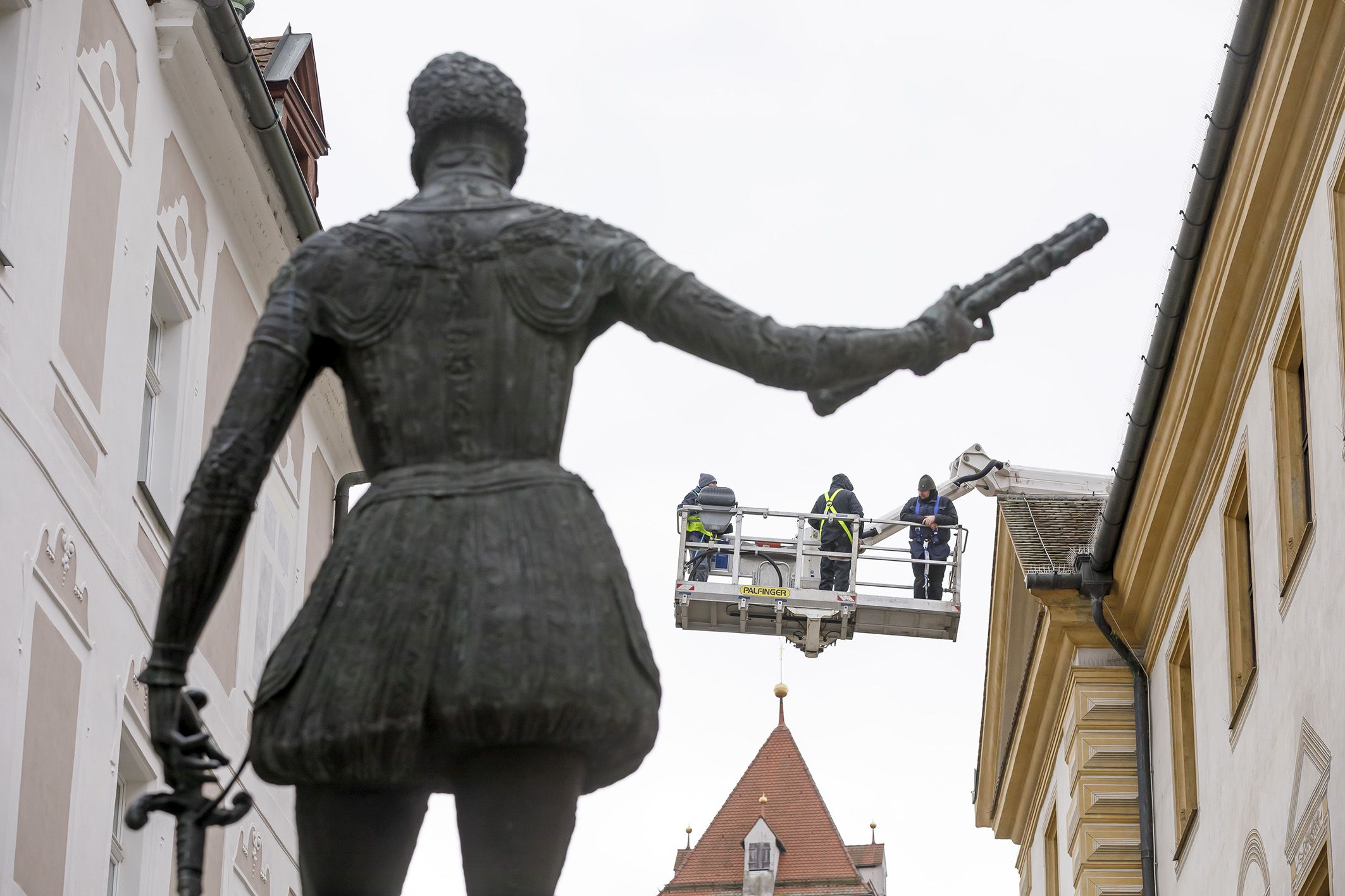Fotografie: Hinter der Statue des Don Juan d'Austria stehen Arbeiter auf einer Hebebühne und begutachten die Fassade des Alten Rathauses.