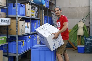 Fotografie: Jakob Pfreimer trägt einen Karton in der Lagerhalle.