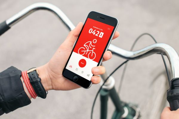 Fotografie: Eine Hand hält ein Smartphone über einem Fahrradlenker. Auf dem Smartphone ist die DB Rad+ App geöffnet.