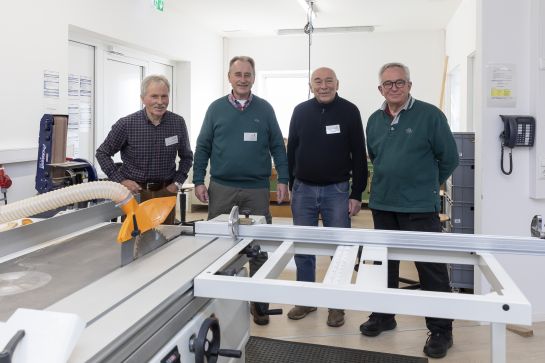 Fotografie: Vier Männer stehen in einer Werkstatt.