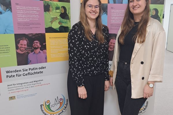 Fotografie: Die Integrationslotsinnen Nadine Sandner-Neumann und Iris Wittmann vor Werbeaufstellern für das Patenschaftsprojekt