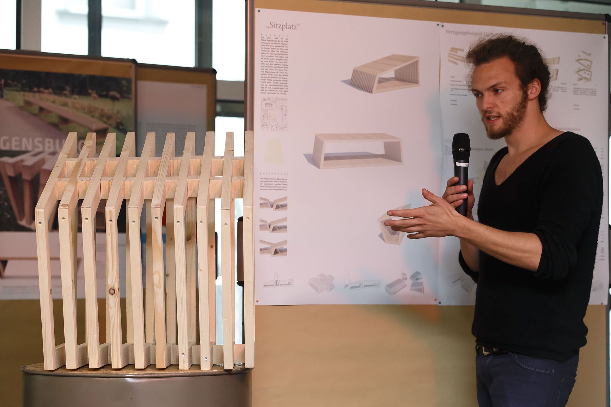 Aktion Sondermöbel - Foto einer Veranstaltung - vor einer Infowand und einem Modell eines Sitzplatzes am Mikrofon Simon Stolz
