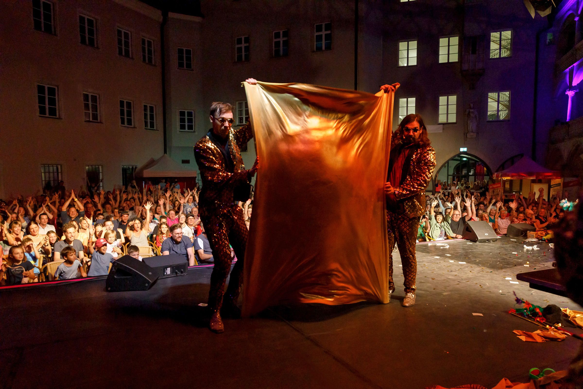 Fotografie: Die Künstler Siegfried und Roy spannen ein Tuch vom Boden nach oben. Im Hintergrund jubelt das Publikum.