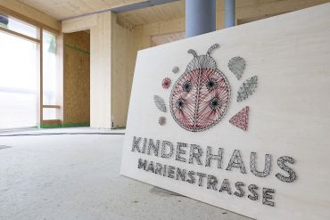 Fotografie: Ein Holzschild mit dem Schriftzug „Kinderhaus Marienstraße“ aus Drähten