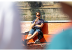Fotografie: Ein Besucher sitzt mit einem Getränk auf gekippten Bierbänken und hat die Schuhe ausgezogen.