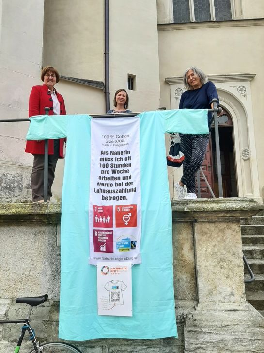 Fotografie: Mit einem überdimensionalen T-Shirt machte die Fairtrade-Steuerungsgruppe bei der Nachhaltigkeitswoche auf die Missstände in der Modeindustrie aufmerksam (v. l.: Gisela Niklas-Eiband, Iris Eibl und Sabine Leistner). 