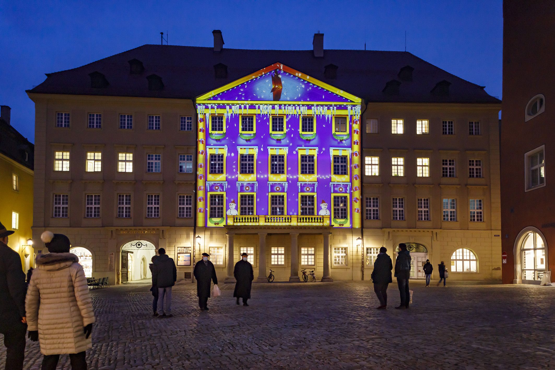 Foto des Monats - Dezember 2020 - Bunt beleuchtetes Gebäude mit Menschen davor