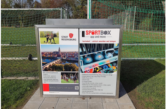 Fotografie - Sportbox auf einem Sportplatz, dahinter Fußballtore