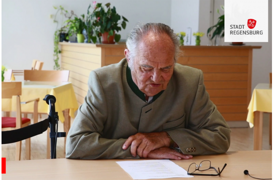 Ein Mann sitzt an einem Tisch und liest von einem Blatt.