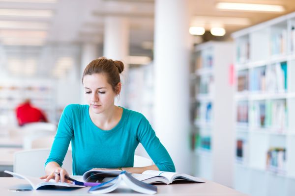 Fotografie: Eine Frau sitzt mit Büchern an einem Tisch.