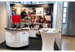 Fotografie - Messestand der Stadt Regensburg - im Vordergrund ein Stehtisch und ein Counter, im Hintergrund eine Bilderwand mit Fotos städtischer Bediensteter (C) Stadt Regensburg, Thomas Fischer