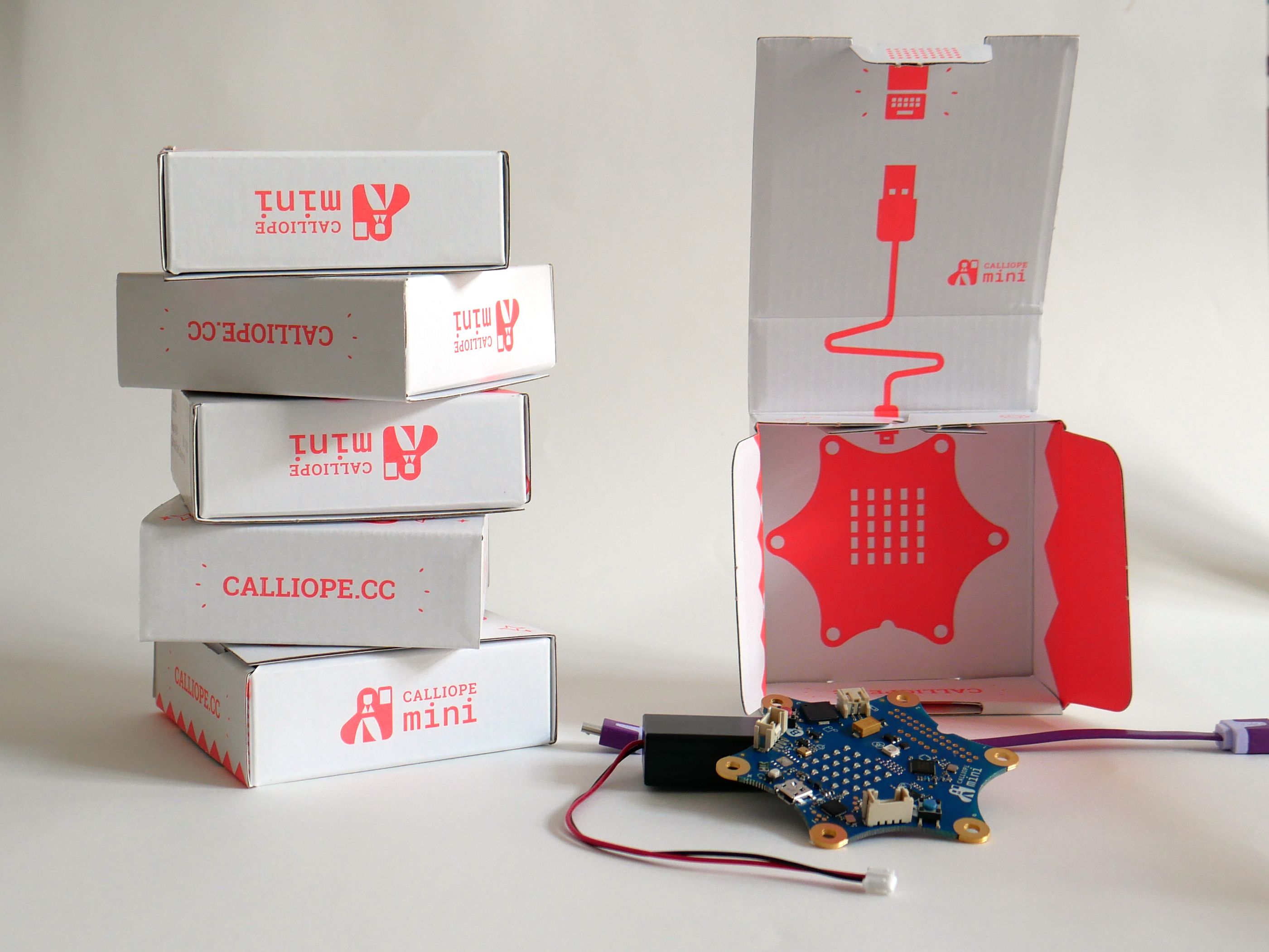 Ein programmierbarer Calliope Mini, ein Mikro-Controller, der aussieht wie ein Stern, neben leeren Calliope-Schachteln.