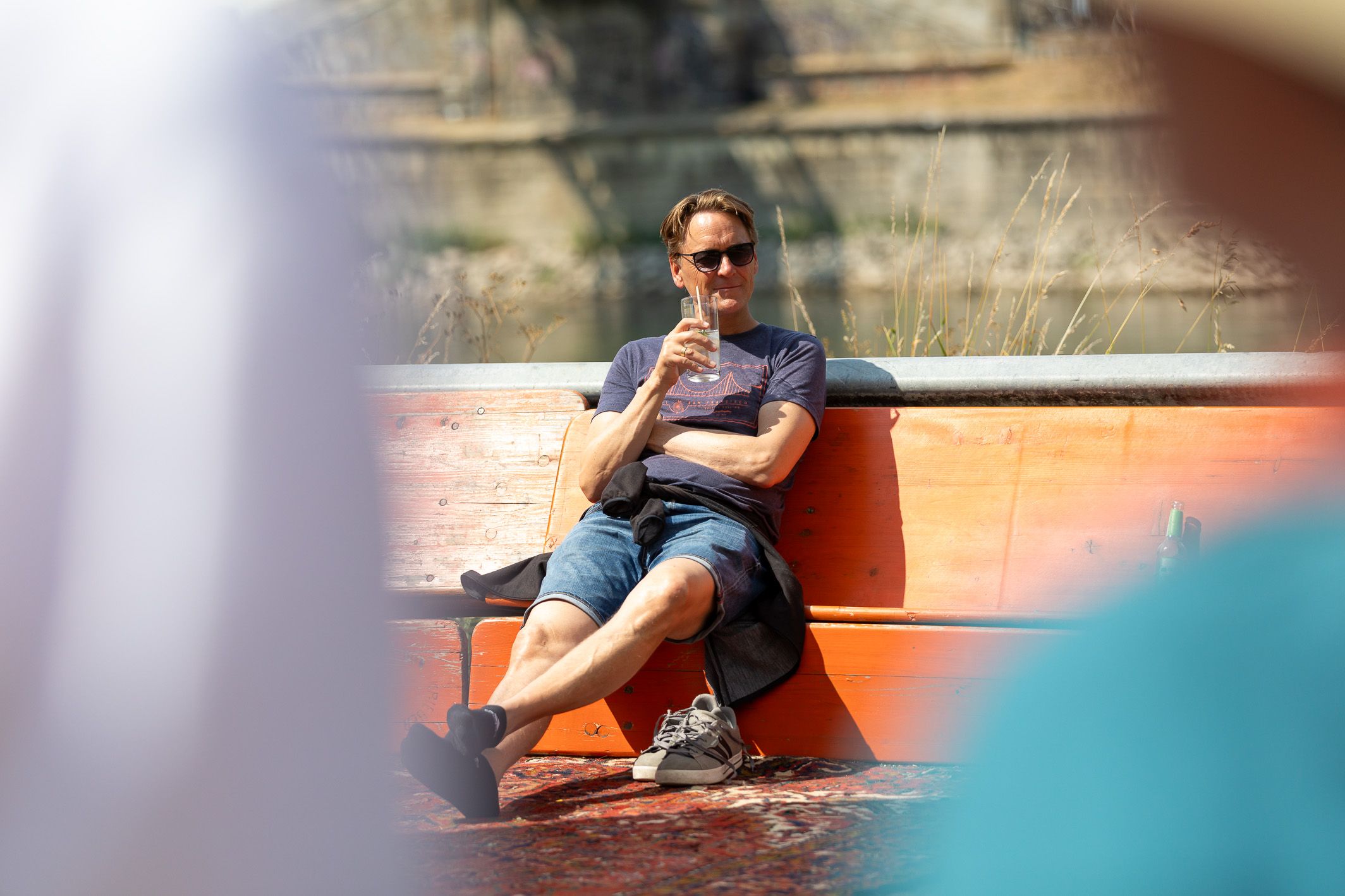 Fotografie: Ein Besucher sitzt mit einem Getränk auf gekippten Bierbänken und hat die Schuhe ausgezogen.
