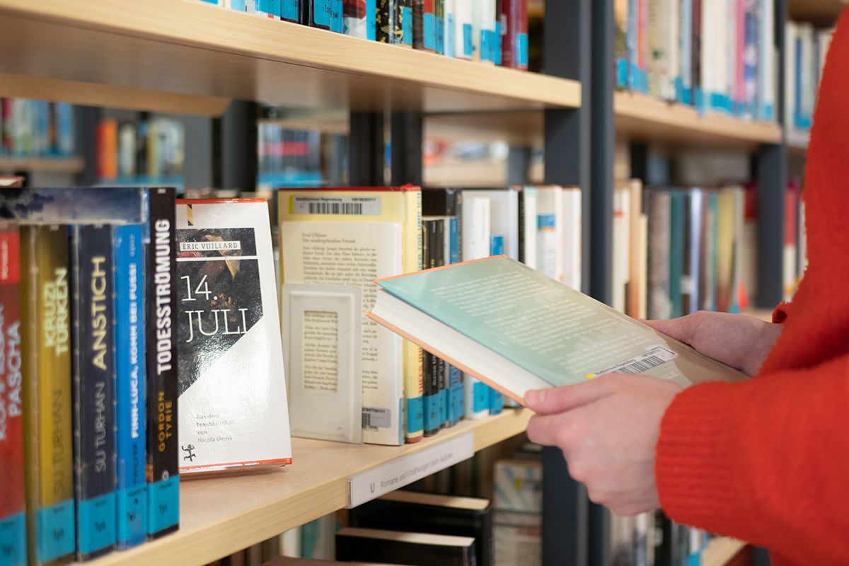 Fotografie - Eine Person liest sich den Buchrücken eines Romans durch.
