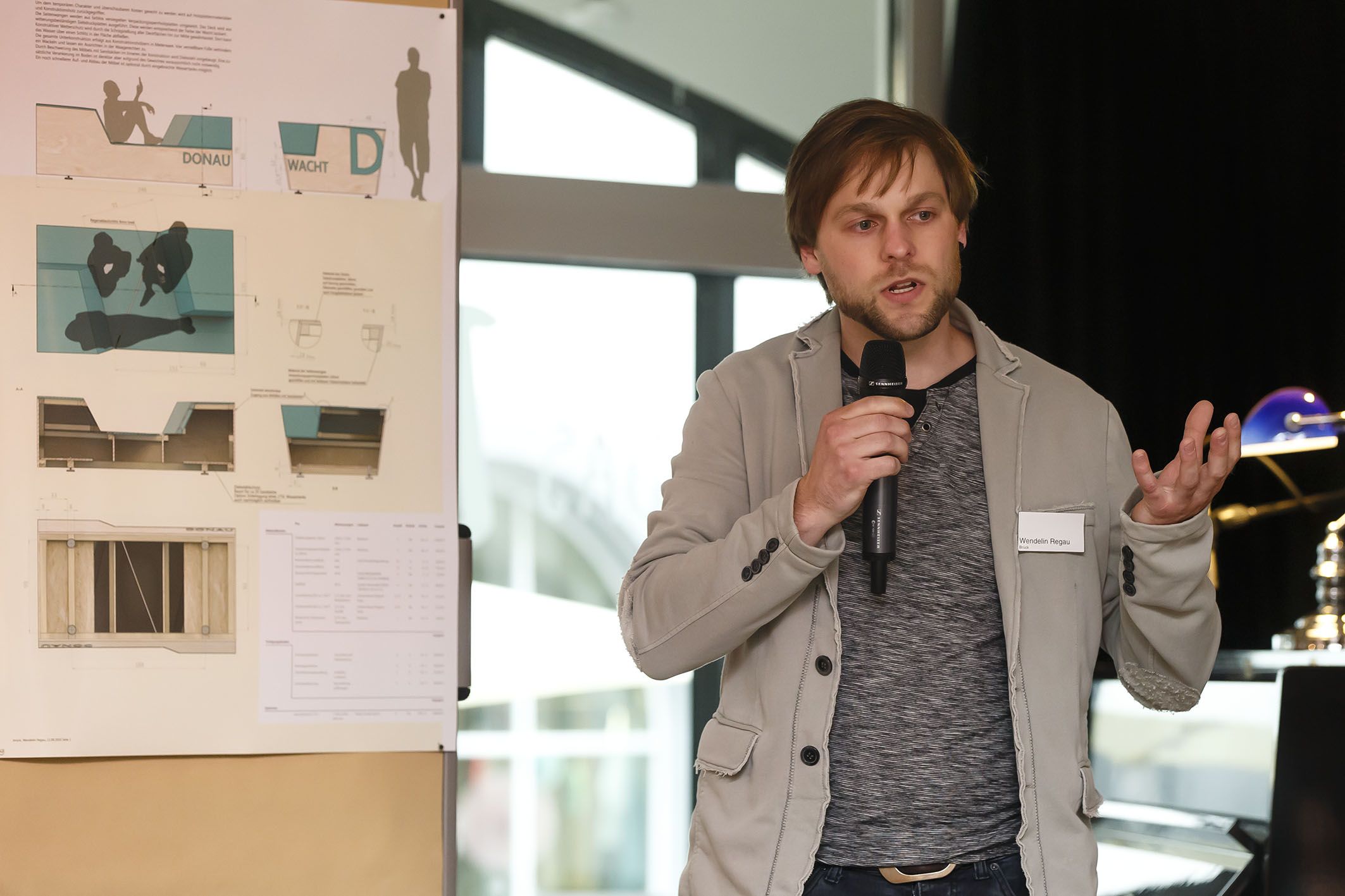 Aktion Sondermöbel - Foto einer Veranstaltung - vor einer Infowand am Mikrofon Wendelin Regau