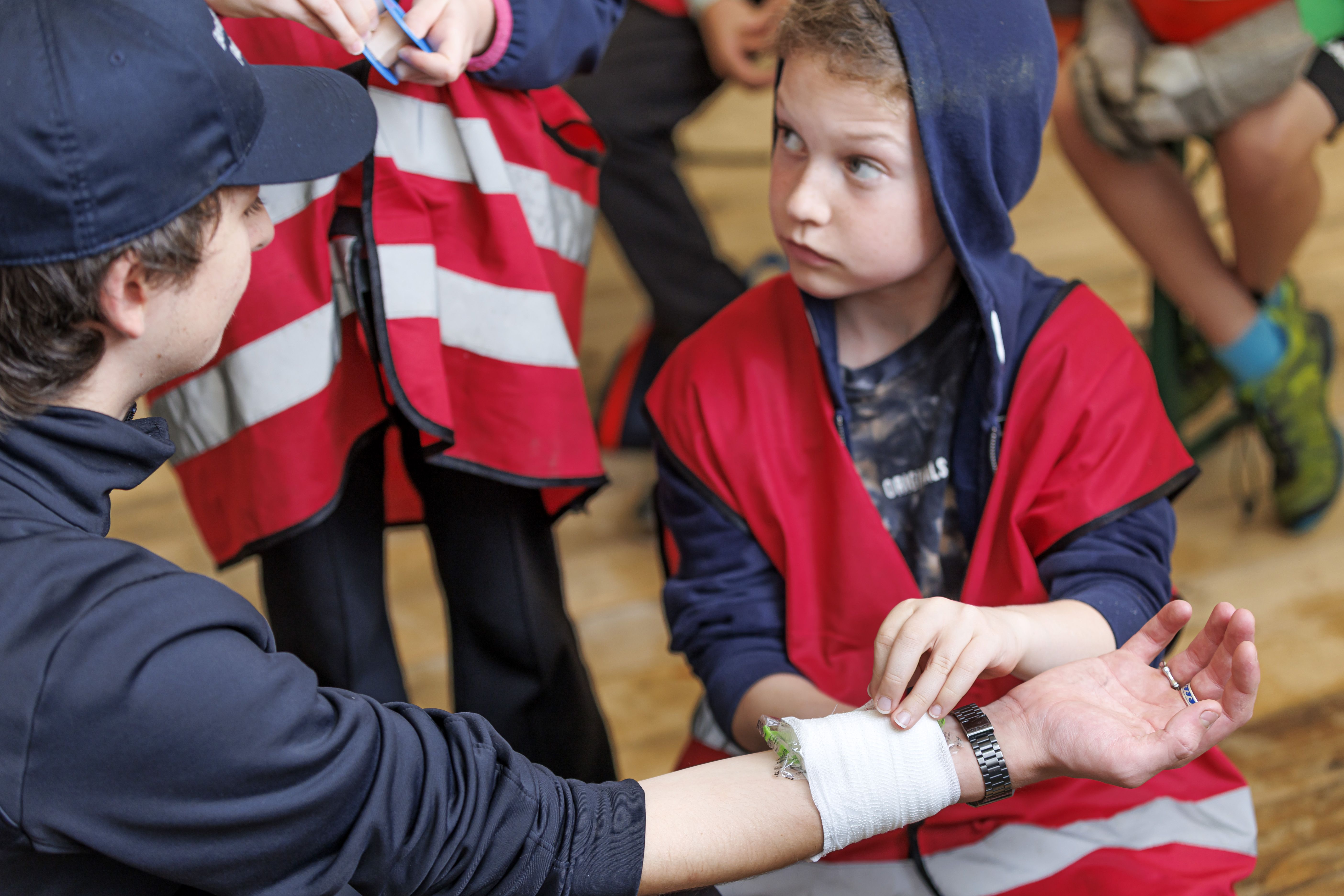 Fotografie: Ein Mini-Feuerwehrmann legt einem Jugendlichen ein Kühlkissen auf den Unterarm. 