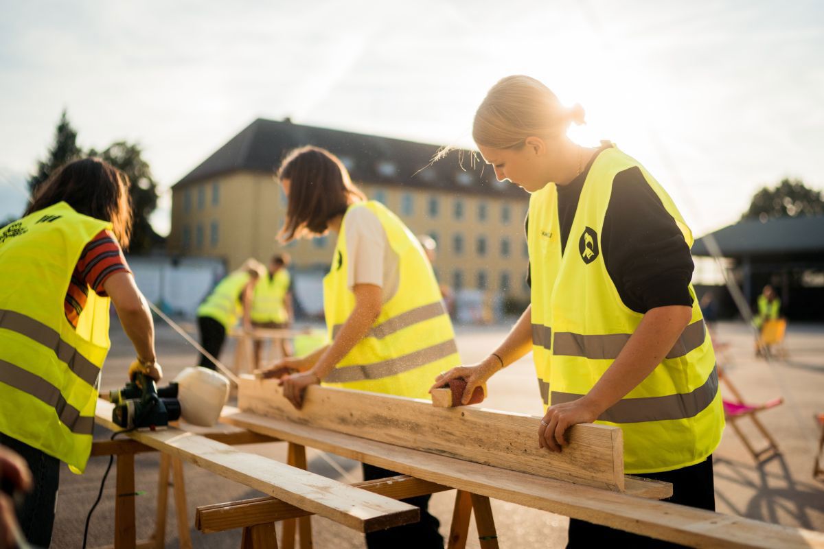 Fotografie – Vorbereitungsarbeiten für Veranstaltungen der PrinzLeoKultur, drei junge Frauen bei der Arbeit an Holzbalken