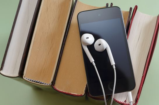 Fotografie - ein Smartphone mit Ohrenstöpseln liegt auf einem Stapel Bücher