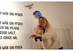 Fotografie – Paulina Grünewald steht auf einer Leiter vor einem Gedicht an der Wand