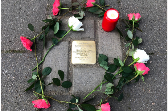 Erinnerungskultur - Stolperstein mit Blumen und einer Kerze