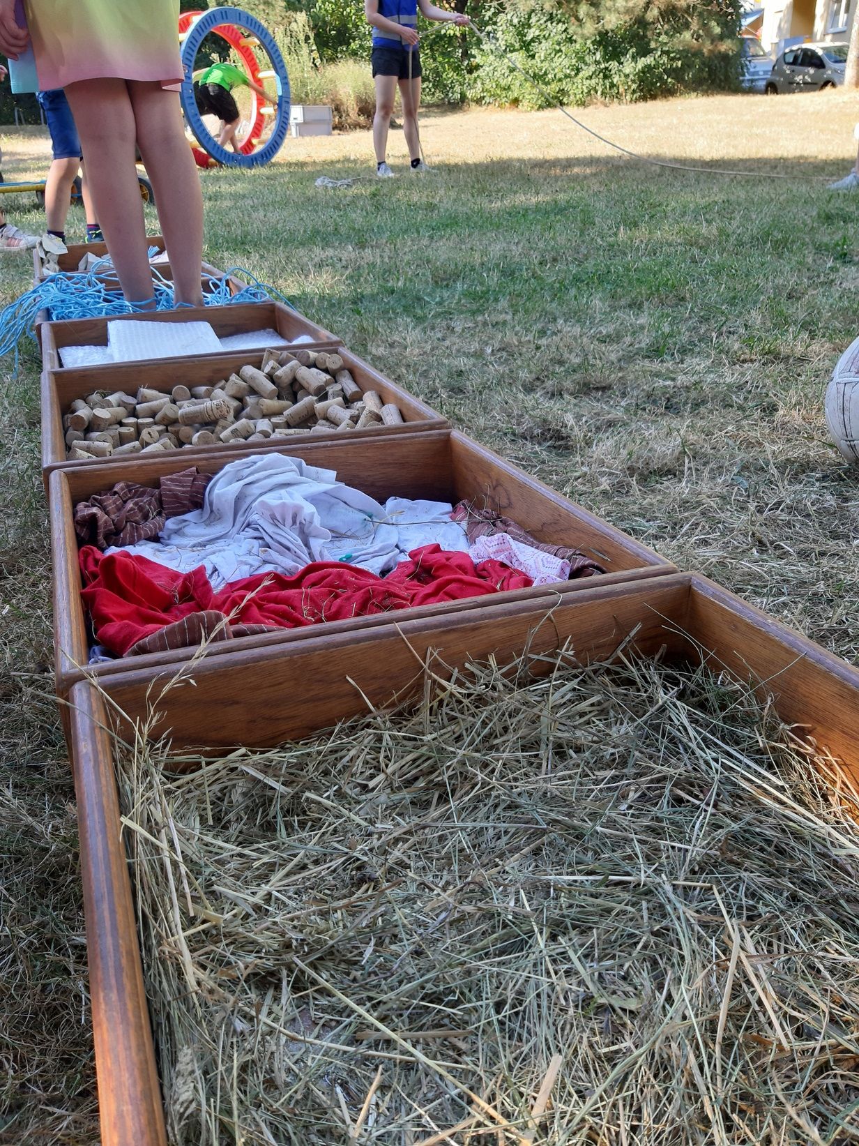 Fotografie – Dunkle Holzkisten gefüllt mit verschiedenen Materialien. In einer Kiste steht ein Kind