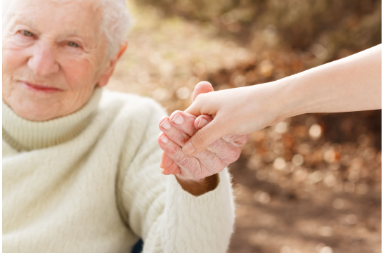 Fotografie: Eine ältere Dame wird an der Hand gehalten.