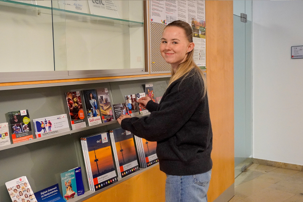 Fotografie -Junge Frau stellt Informationsbroschüren in ein Regal in einem öffentlichen Gebäude der VHS.