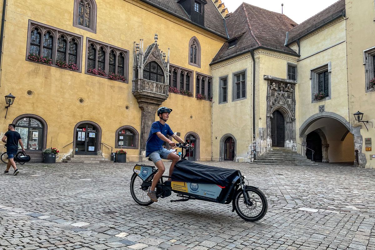 Fotografie: Ein junger Mann fährt mit einem E-Lastenrad über den Rathausplatz.