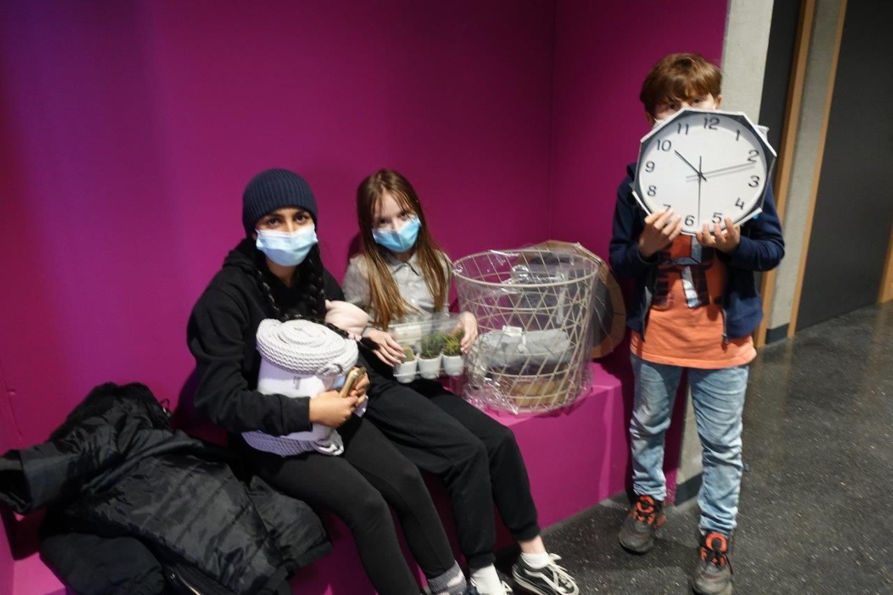 Auf dem Foto sind drei Kinder zu sehen, welche verschieden Gegenstände zeigen. 