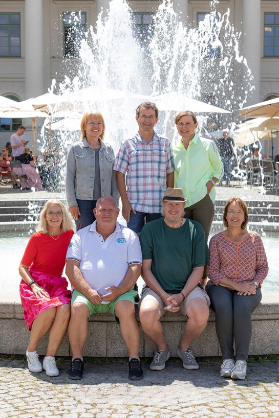 Sieben Personen sitzen vor einem Brunnen.