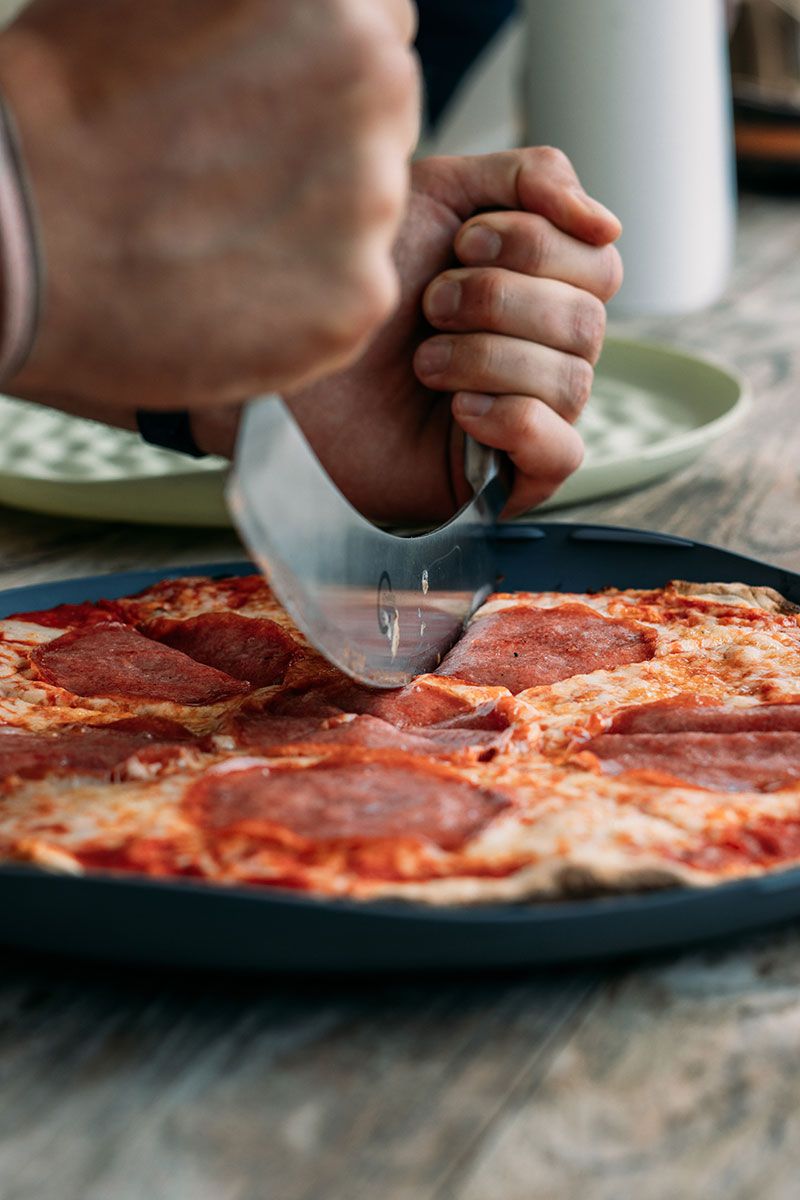 Fotografie - Pizza wird in der wiederverwendbaren Pizzabox aufgeschnitten