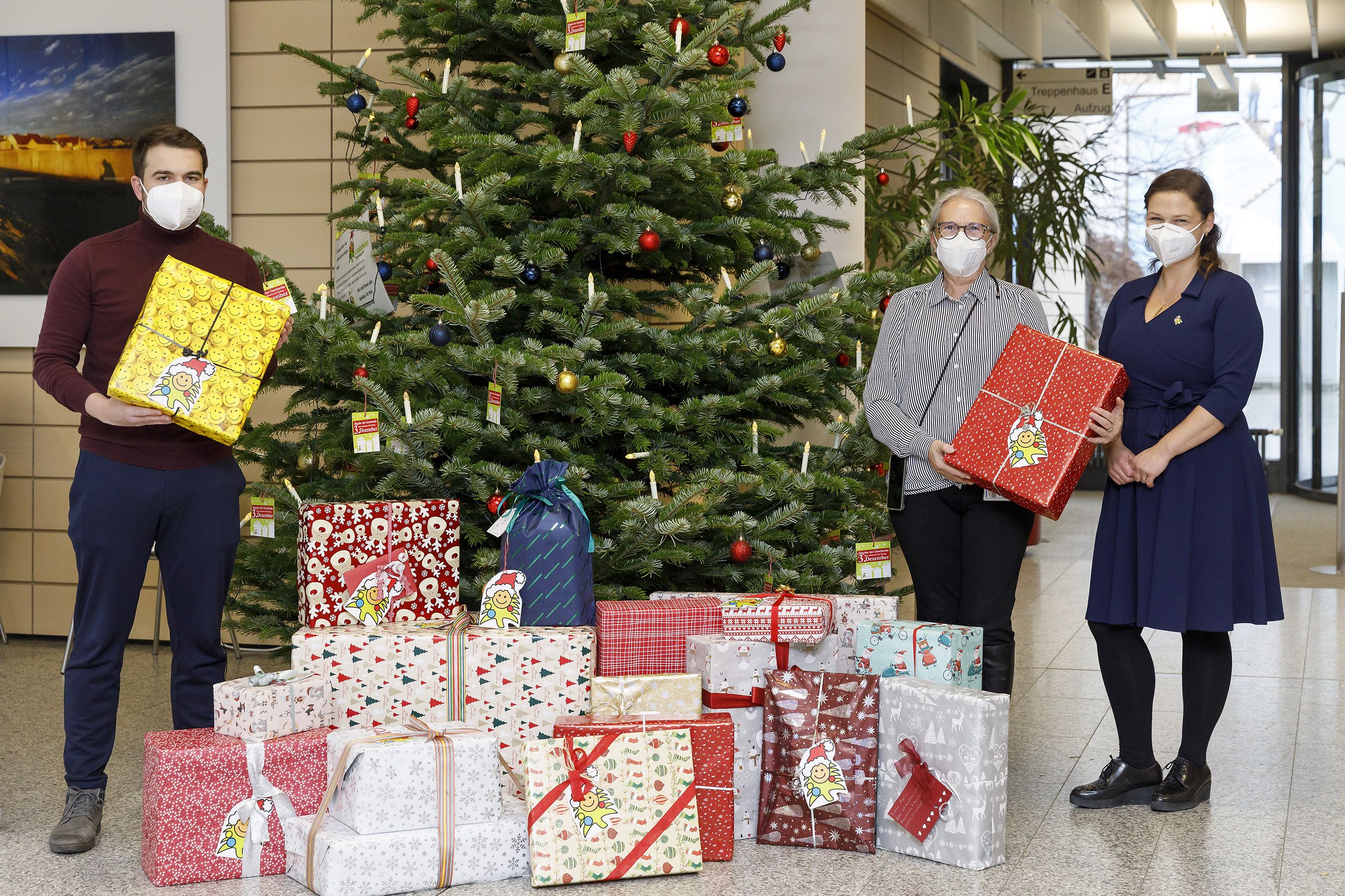Fotografie - drei Personen neben einem Weihnachtsbaum mit Geschenken