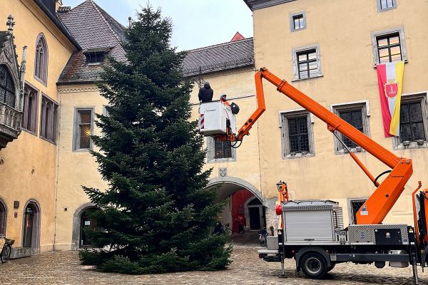 Fotografie: Zwei Männer heben mit einem Hubsteiger den Weihnachtsstern auf den Christbaum am Rathausplatz.