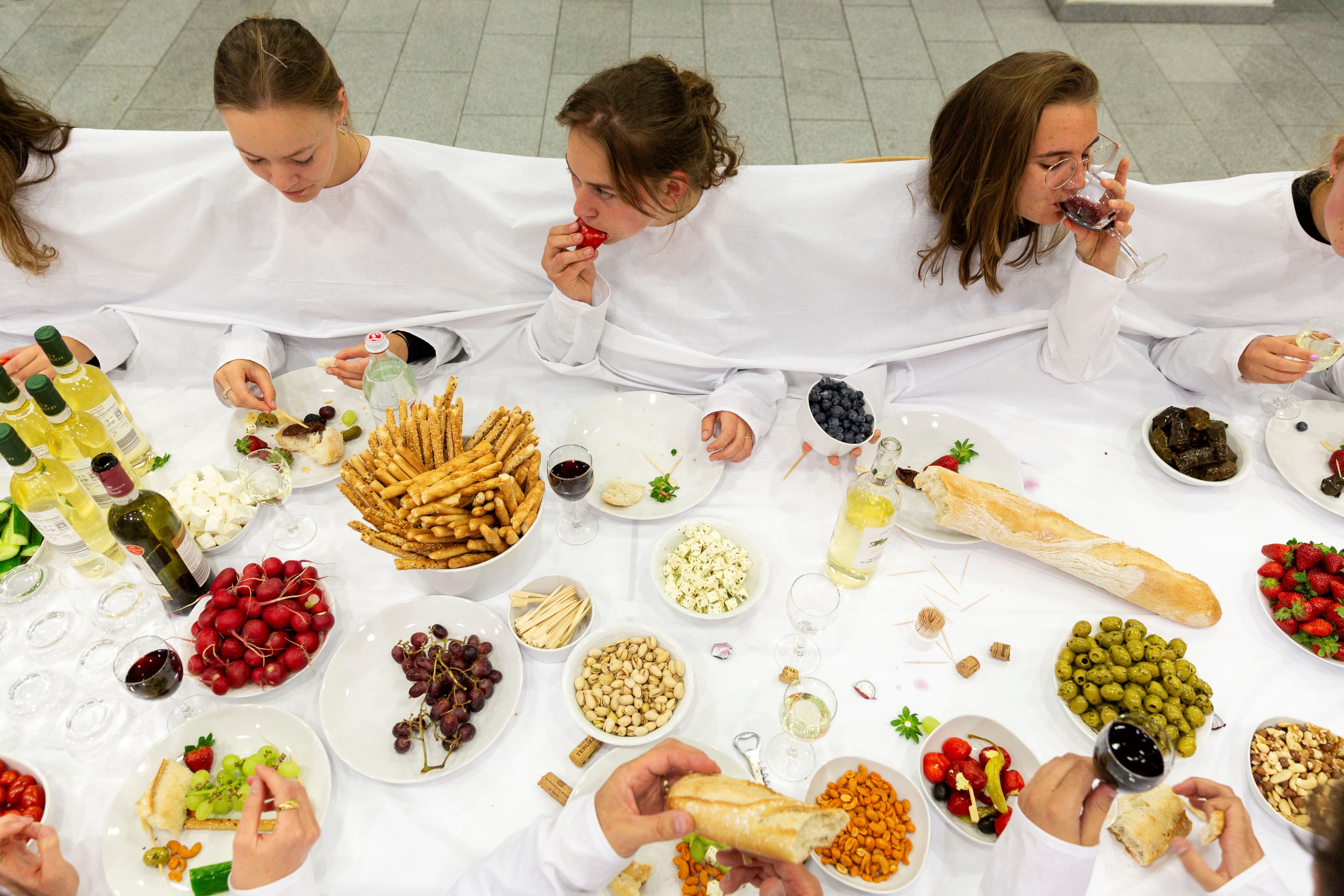 Fotografie: Junge Menschen sitzen zum gemeinsamen Abendessen an einer weißgedeckten Tafel.