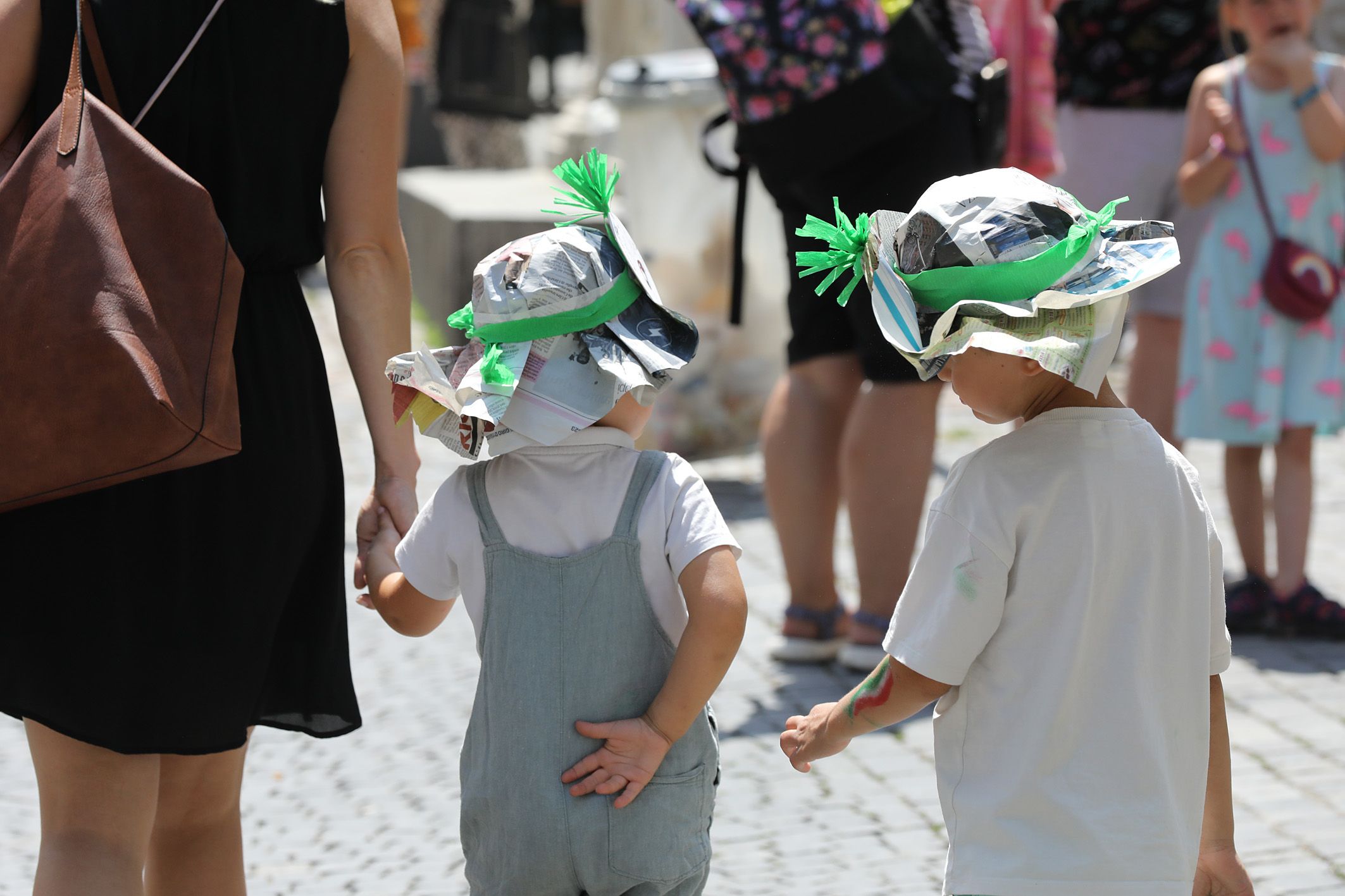 Fotografie: Zwei kleine Kinder mit aus Zeitungspapier und grüner Schleife gebasteltem Kopfschutz