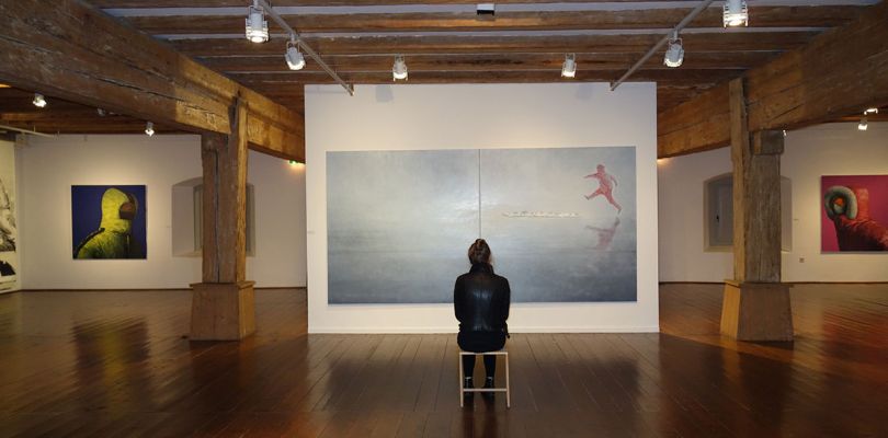 Themenbild Museen - Eine Frau sitzt vor einem großen Gemälde in einer Bilderausstellung
