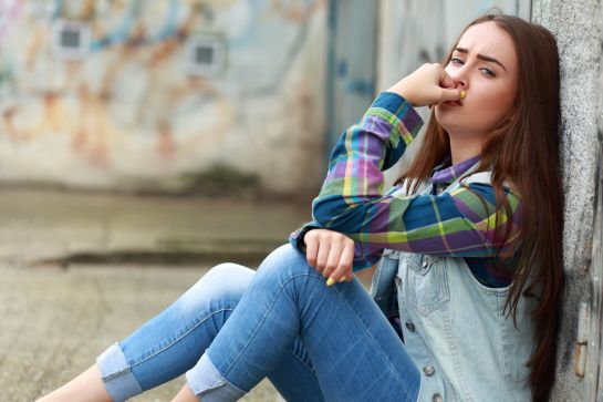 Fotografie: Jugendliche sitzt auf dem Boden an eine Mauer gelehnt