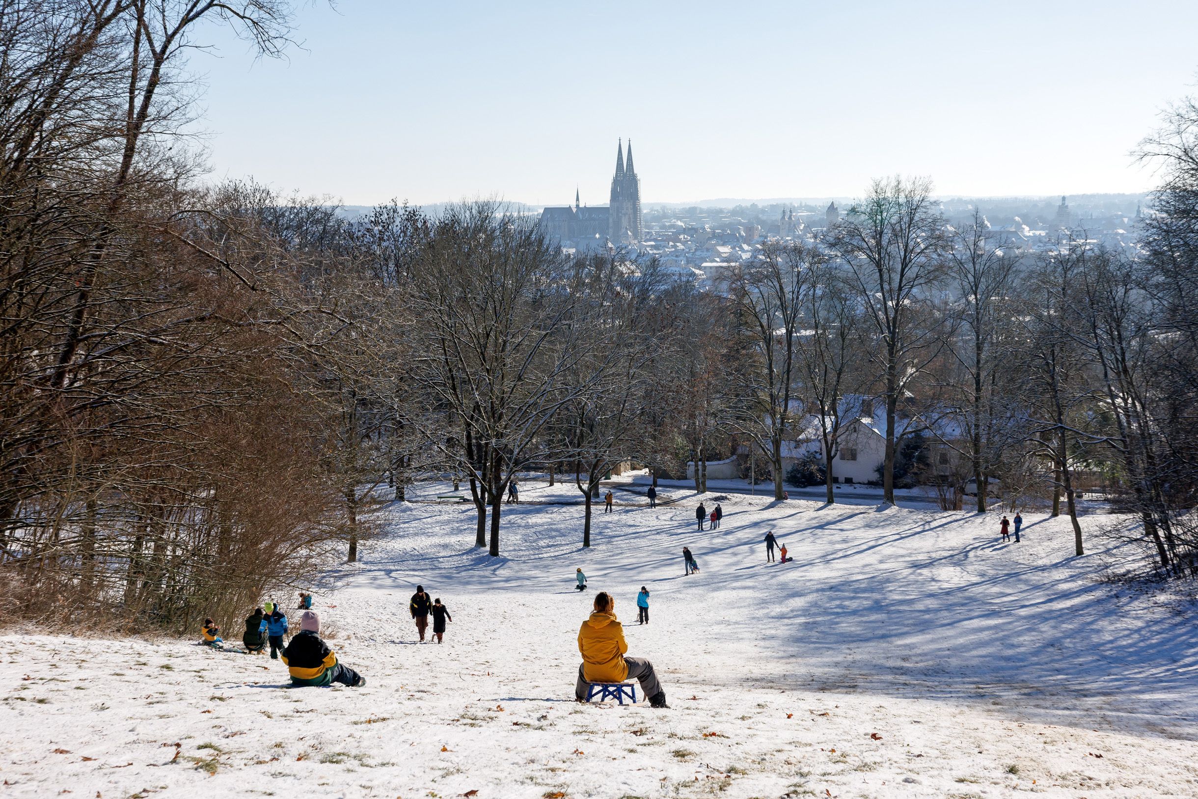 Fotografie: Kinder und Erwachsene fahren den Schlittenberg an der Seidenplantage hinunter, im Hintergrund ist der Dom zu sehen.