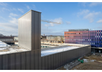 Fotografie - im Hintergrund Rohbau ist der Fahrzeughalle zu sehen, rechts davon der Neubau der Hauptfeuerwache; im Vordergrund bereits fertiggestellte Fahrzeughalle mit Schlauchturm