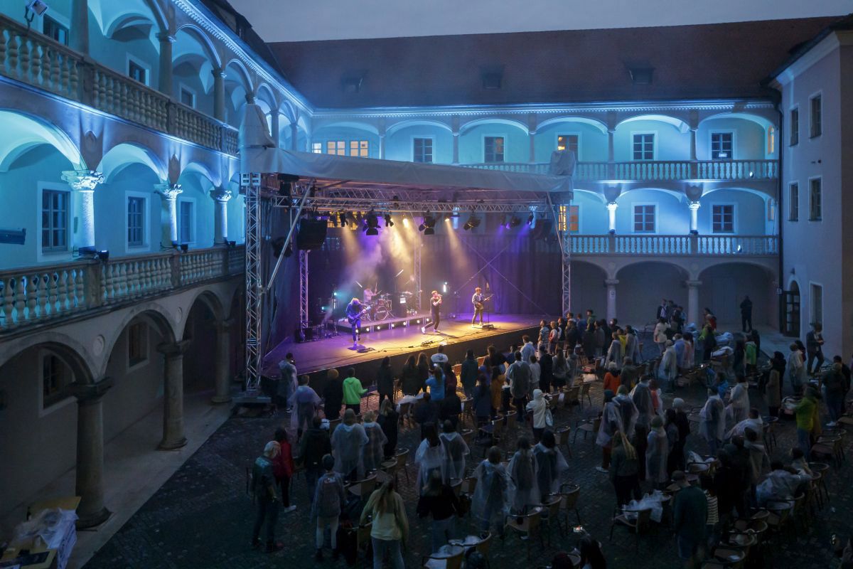 Fotografie – Konzert im blau beleuchteten Innenhof des Thon-Dittmer-Palais in Regensburg, Zuhörende und beleuchtete Bühne